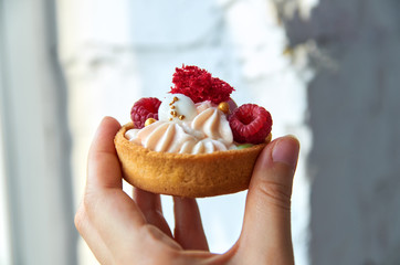 Homemade muffin in a brown sugar basket with white cream and fresh red raspberry in hand on blurred gray background close up. Side view