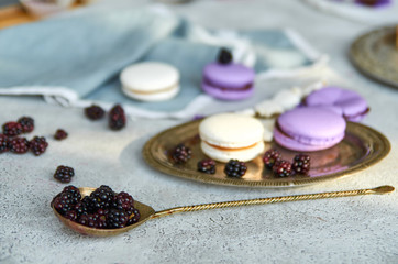 Vintage spoon with fresh blackberries in the foreground. On a blurred gray background macarons and fresh blackberries. Side view