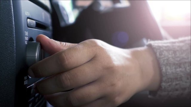 Close-up of female hand adjusting button audio on a vehicle's dashboard.