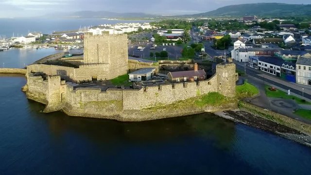 Medieval Norman Castle in Carrickfergus near Belfast in sunrise light. Aerial video with marina, yachts, parking, town and far view of Belfast in the background