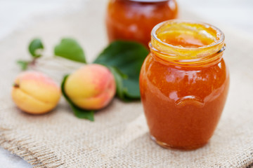 Apricot jam in glass jars with fresh fruit on table