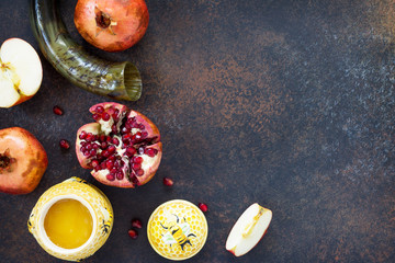 The concept of Rosh hashanah (Jewish New Year). Traditional holiday symbols - shofar, honey, apple and pomegranate on a stone or slate background. Flat lay, top view.