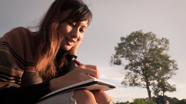 Young woman with pen writing on notebook at nature.