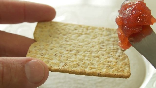 Spreading Jam on a whole wheat cracker for breakfast with a knife. Close up, day, 4k.