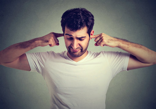 angry annoyed man plugging his ears with fingers