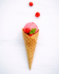 Raspberry ice cream in cone with fresh raspberry and peppermint leaves setup on white wood background . Summer and Sweet concept flat lay.