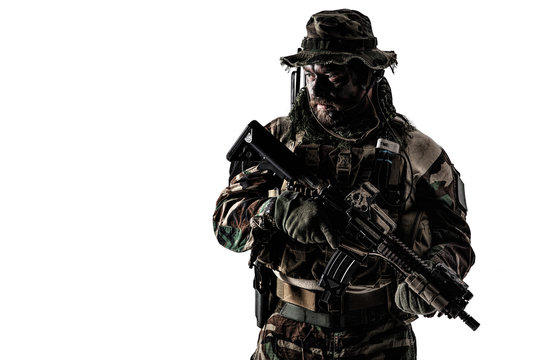 Special forces United States in Camouflage Uniforms studio shot. Holding weapons, wearing jungle hat, Shemagh scarf, painted face, he is ready to kill. Dark contrast