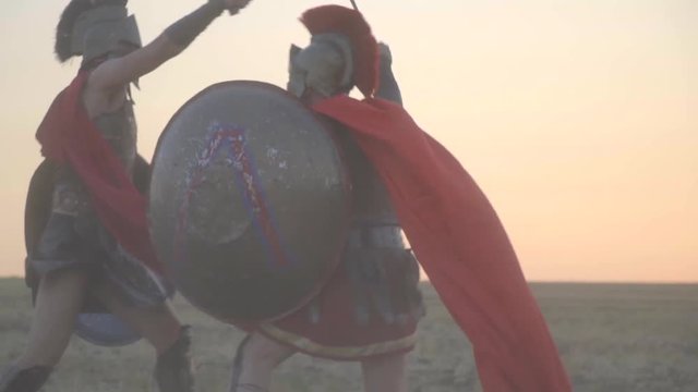 Two powerful Roman gladiators are fighting in the open field, evading each other's attacks, slow motion