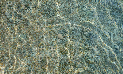 Fototapeta na wymiar Shimmering sun glares on pebble seabed under water as background.
