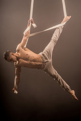 circus artist on the aerial straps with Strong muscles on the background of smoke