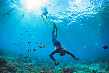 Happy family vacation. Man in snorkeling mask with camera dive underwater with tropical fishes in...