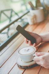 Woman using smartphone with a cup coffee in coffee shop cafe with vintage color tone filter background