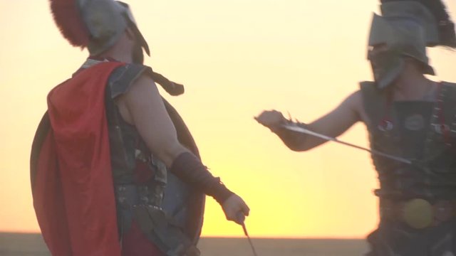 The gladiator beats off the attack with a sword and hits another gladiator in the ear, filming against the dawn in the field, slow motion