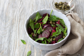 Beetroot salad with baked red onion, capers, watercress, greens and vinaigrette sauce. Vegan healthy food. In a blue bowl on a wooden table