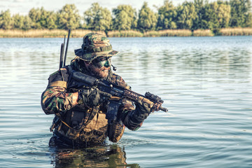 Bearded soldier of special forces in action during river raid in the jungle terrain. He is waist...