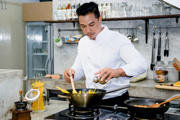 Asian chef is cooking food by using wooden ladle at the kitchen of a restaurant