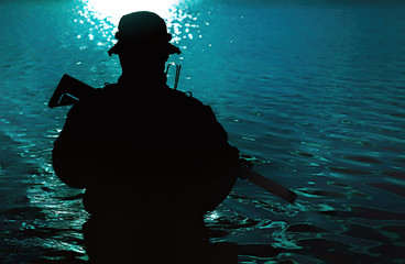 Silhouette of special forces with rifle in action during river raid in the jungle waist deep in the...
