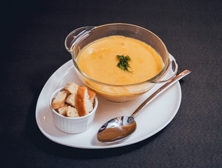 Pumpkin and carrot soup with cream and parsley on dark background.