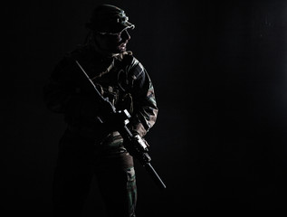 Fototapeta na wymiar Bearded Special forces United States in Camouflage Uniforms studio shot half length. Holding weapons, wearing jungle hat, Shemagh scarf, he is ready to kill. Contour shot, backlit