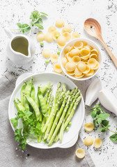 Ingredients for vegetarian lunch - orecchiette pasta, green peas, asparagus, cream on a light background, top view