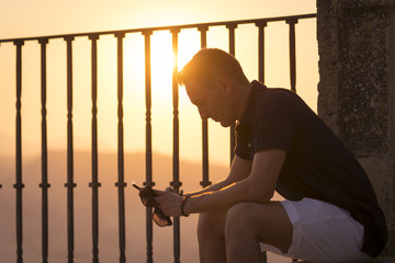 Fototapeta premium Young male siting and looking his phone at sunset