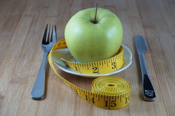 Apple with fork, knife and measure tape in a dish
