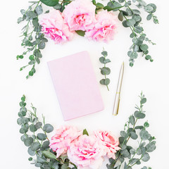 Floral frame of rose flowers and eucalyptus branches with notebook and pen on white background. Flat lay, top view