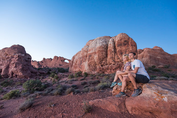 Fototapeta na wymiar Young couple sitting on rock in front of skyline arch in national park at twilight