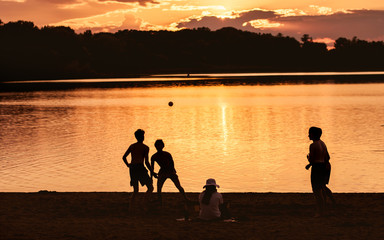 A group of young boys are play softball on a beach under sunset