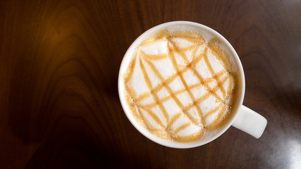 Top view of hot coffee latte art caramel foam in ceramic cup on wooden table background