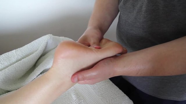 Foot massage in beauty salon, close up view. Woman having sports foot massage in spa salon. Male masseur therapist hands doing on female foot massage. Professional masseuse massaging foot of girl.