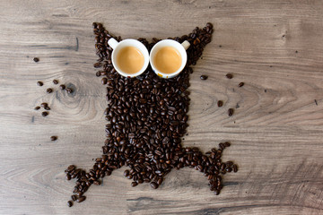 Owl shaped figure made out of coffee beans and two full espresso cups on top of a wooden table