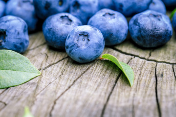 Freshly picked blueberries on a stump at the garden. Juicy and fresh blueberries with green leaves on rustic wooden surface. Concept for healthy eating and nutrition.