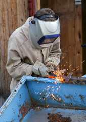 A young welder at work. The worker is engaged in welding parts of the car trailer