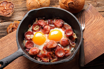 Fried eggs with sausage and onion on frying pan