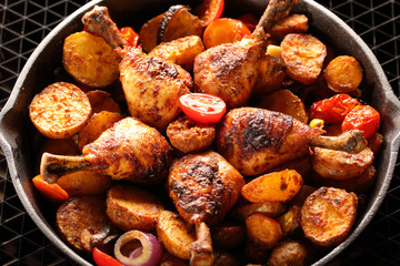 Roasted chicken legs with baked potato on frying pan