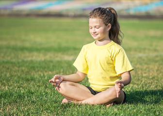 A young, pretty little girl with long hair doing yoga exercises. Lotus asana. Copy-space