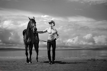 Macho man handsome cowboy and horse on the background of sky and water.