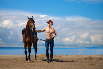 Macho man handsome cowboy and horse on the background of sky and water.