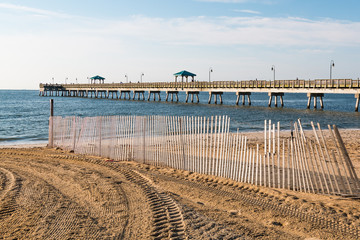 A sand fence lies along Buckroe Beach in Hampton, Virginia, with a view of the fishing pier in the background.