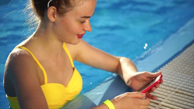 A young and embroidered woman who wore a swimsuit is in the pool with cool water, a beautiful woman looks at photos on a mobile phone for social networks