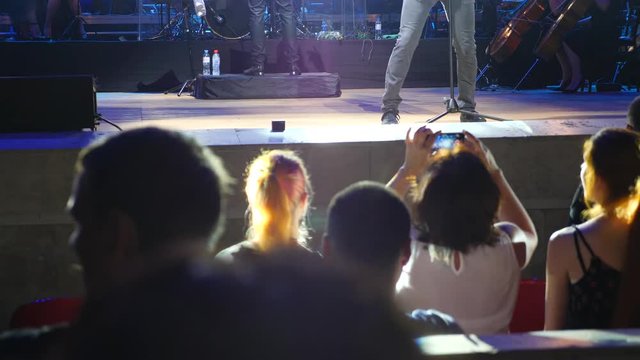 A crowd of people lit by colorful light during a concert of a rock band with a symphony orchestra. 4k. Slow motion