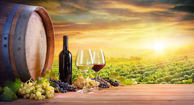 Wine Glasses And Bottle With Barrel In Vineyard At Sunset

