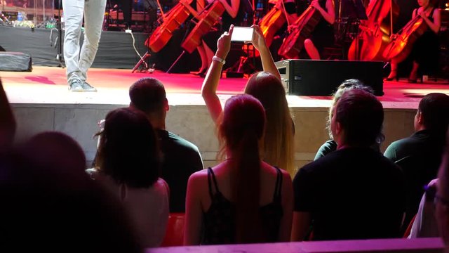 Viewers shoot video on smartphones during a concert of a rock band with a symphony orchestra. 4k