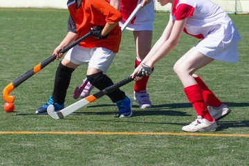 Fototapeta na wymiar Children playing field hockey competitively. Two defender girls challenging boy attacker