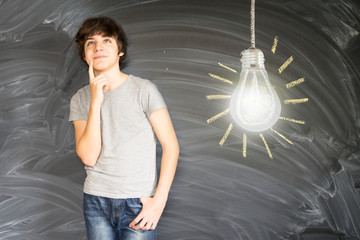Teenager boy against getting an idea blackboard with glowing lightbulb background