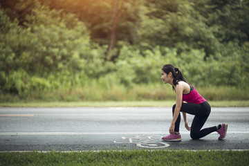 young woman runner tying shoelace on country road