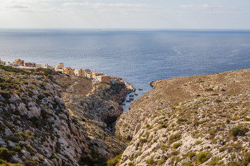 Fototapeta na wymiar Limestone rocks covered by exotic plants - coast of Malta island. Small town on the rock