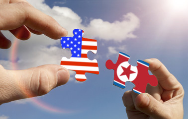 puzzles in the form of flags of North Korea and USA of America in the hands of people against the sky