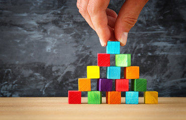 man's hand holding a top of wooden blocks pyramid over wooden table